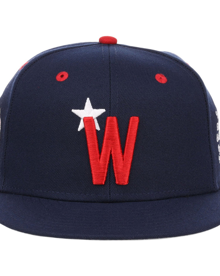 The Ebbets Field Washington Black Senators NLB Varsity Fitted Ballcap is navy with a red brim button, red ventilation holes, and features a large red 