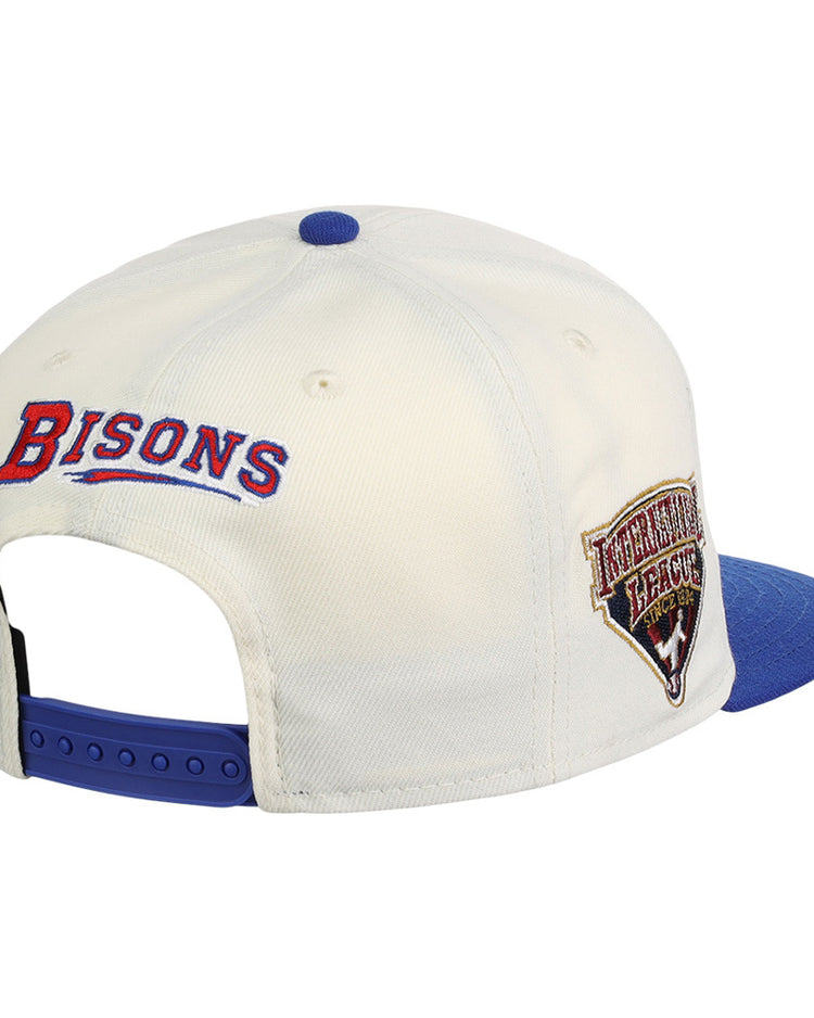 The Buffalo Bisons MiLB Snapback Ballcap by Ebbets Field is a white cap with a blue brim, BISONS embroidered in red and blue on the back, and an International League patch on the side.