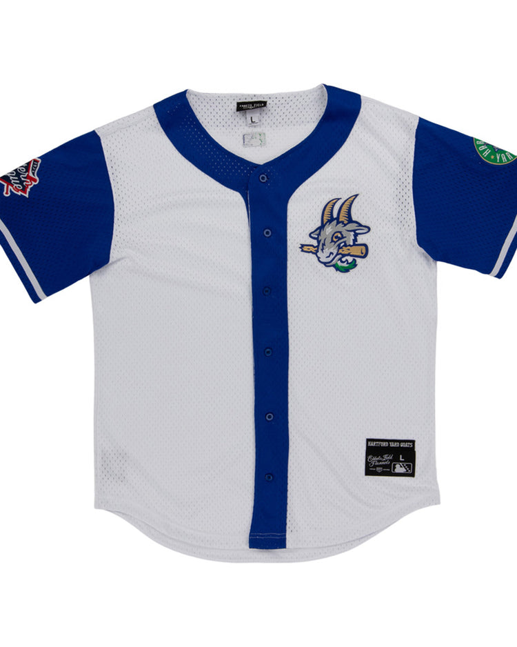 The Ebbets Field Hartford Yard Goats MiLB Button Down Jersey is white with blue sleeves and trim, a cartoon goat logo on the chest, sleeve patches, button-down front, and a black label near the hem.