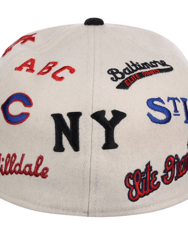 The Ebbets Field Negro League Baseball NLB Ballpark Fitted Ballcap is a white cap embroidered in red, black, and blue with vintage team logos and names like NY, STL, Elite Giants, Hilldale, Baltimore Elite Giants, and ABC.