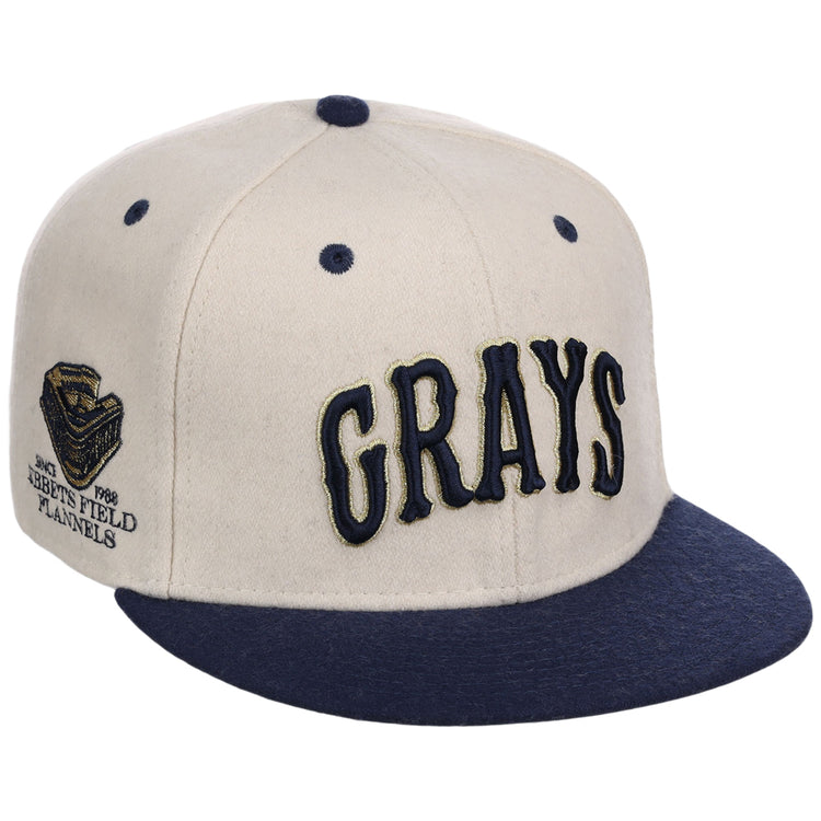 The Ebbets Field Homestead Grays NLB Ballpark Fitted Ballcap features a beige crown, navy blue brim and top button, 