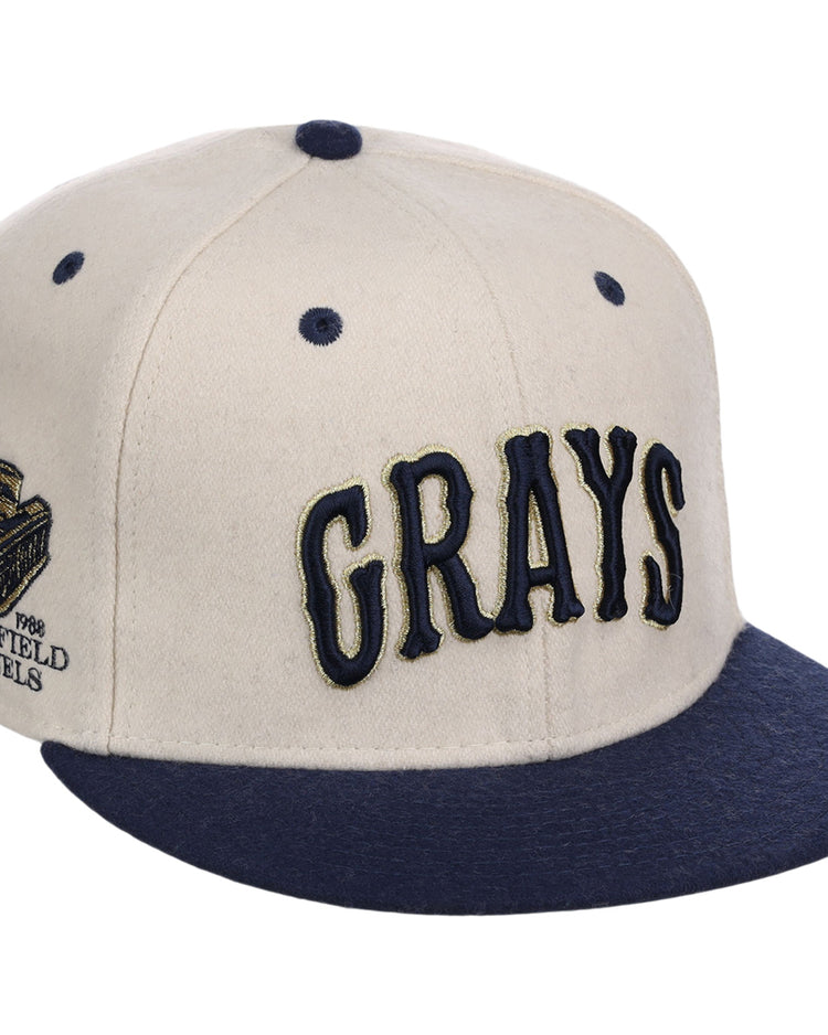 The Ebbets Field Homestead Grays NLB Ballpark Fitted Ballcap features a beige crown, navy blue brim and top button, 