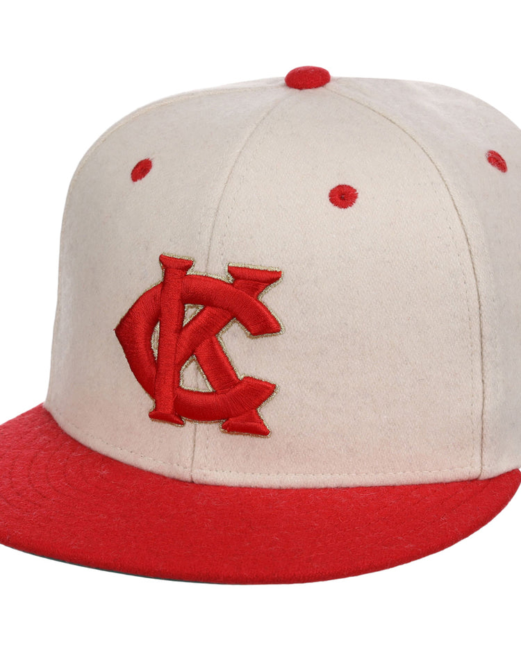 The Kansas City Monarchs NLB Ballpark Fitted Ballcap by Ebbets Field is beige with a red interlocking KC logo on the front, plus red eyelets and a red top button.
