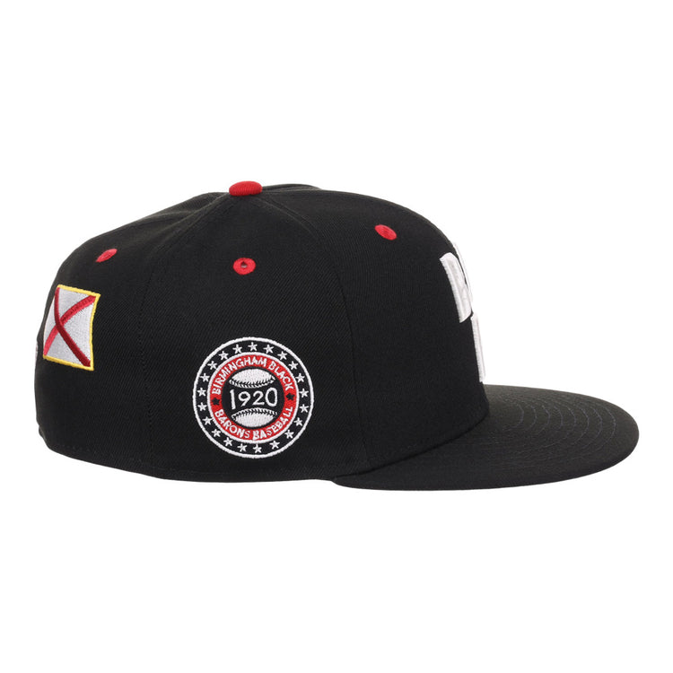 The Ebbets Field Birmingham Black Barons NLB Varsity Fitted Ballcap features a black flat brim, red top button, colorful side patch, and circular embroidered patch reading 