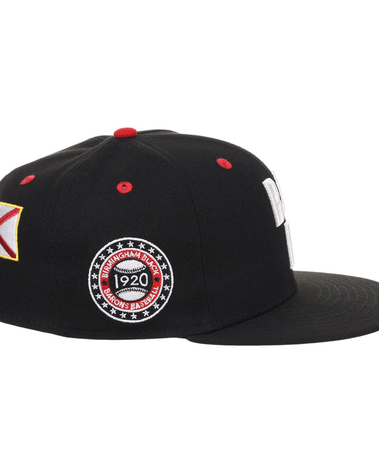 The Ebbets Field Birmingham Black Barons NLB Varsity Fitted Ballcap features a black flat brim, red top button, colorful side patch, and circular embroidered patch reading 
