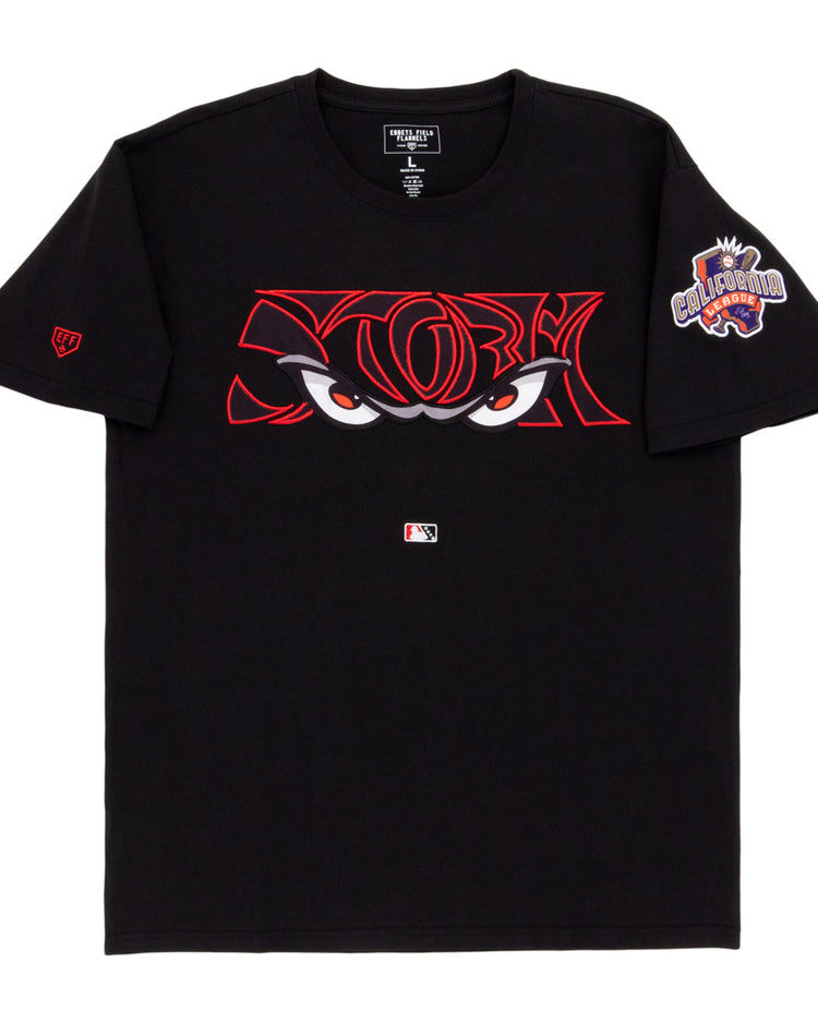 The Ebbets Field Lake Elsinore Storm MiLB Fashion Cotton Short Sleeve Tee is a black shirt with bold red-outlined cartoon eyes on the chest, an MLB logo underneath, and a colorful 