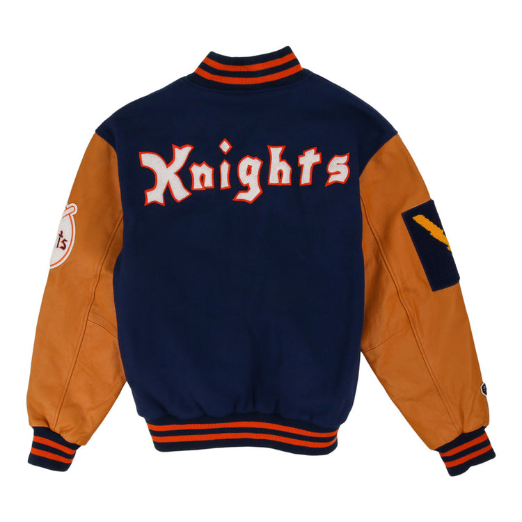 The Ebbets Field New York Knights Dna Varsity Jacket features tan leather sleeves, a navy blue body, striped orange and navy trim, 