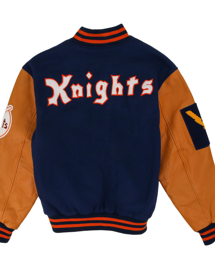 The Ebbets Field New York Knights Dna Varsity Jacket features tan leather sleeves, a navy blue body, striped orange and navy trim, 