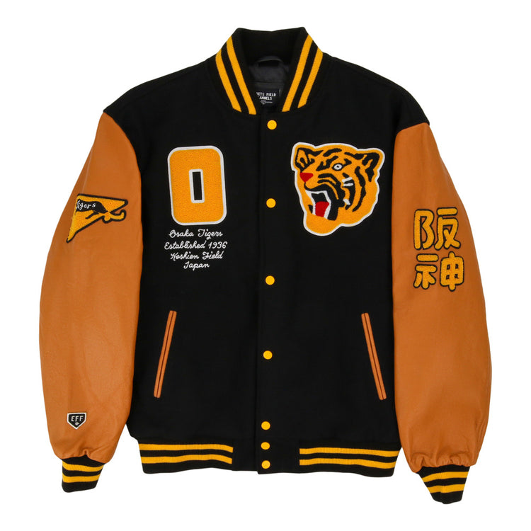 The Ebbets Field Osaka Tigers DNA Varsity Jacket features a black body, tan leather sleeves, yellow and black striped cuffs and collar, tiger face patch, yellow 0, Japanese text, and assorted patches on the front and sleeves.