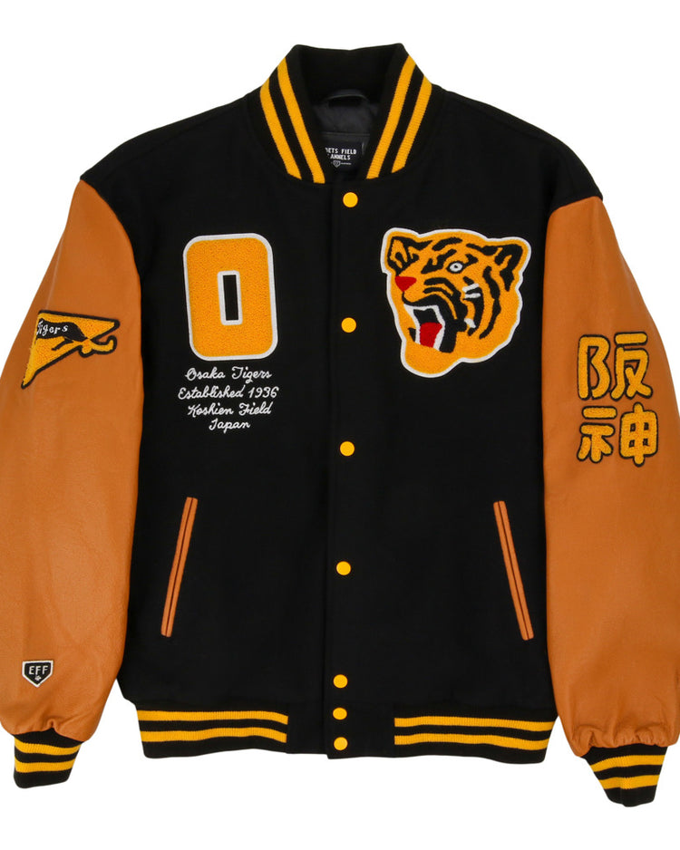 The Ebbets Field Osaka Tigers DNA Varsity Jacket features a black body, tan leather sleeves, yellow and black striped cuffs and collar, tiger face patch, yellow 0, Japanese text, and assorted patches on the front and sleeves.