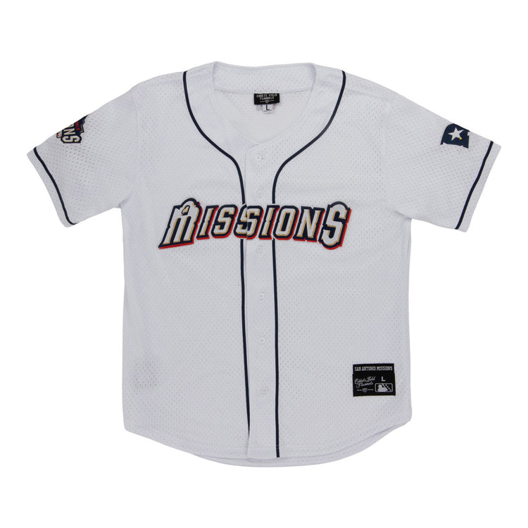 The Ebbets Field San Antonio Missions MiLB Button Down Jersey features “Missions” across the chest, navy blue trim, a Texas flag patch on the left sleeve, and team and brand tags near the bottom hem.