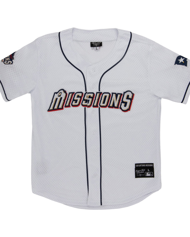 The Ebbets Field San Antonio Missions MiLB Button Down Jersey features “Missions” across the chest, navy blue trim, a Texas flag patch on the left sleeve, and team and brand tags near the bottom hem.
