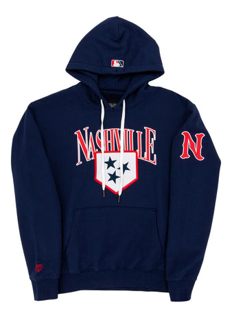 The Ebbets Field Nashville Sounds MiLB Cotton Hooded Sweatshirt is a navy blue hoodie with white drawstrings, Nashville in bold white and red letters, a three-star shield on the chest, red N on the sleeve, and an MLB logo on the hood.
