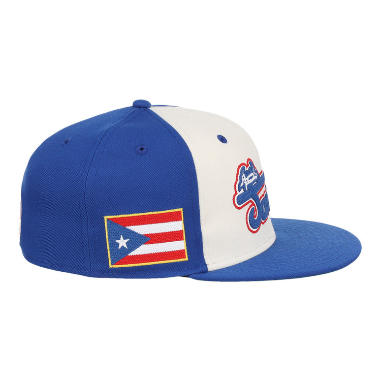The Santurce Cangrejeros Wordmark Chainstitch Fitted Ballcap by Ebbets Field features blue and white panels, a Puerto Rican flag patch on the side, and a red, white, and blue logo on the front.