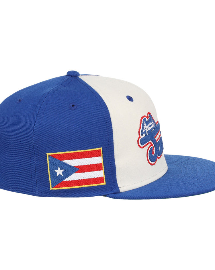 The Santurce Cangrejeros Wordmark Chainstitch Fitted Ballcap by Ebbets Field features blue and white panels, a Puerto Rican flag patch on the side, and a red, white, and blue logo on the front.