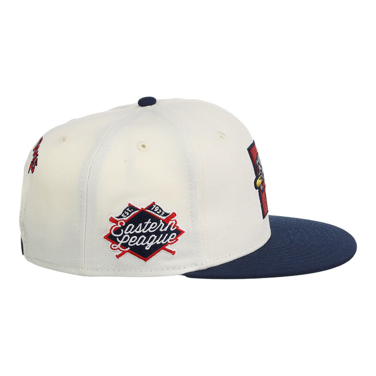The Ebbets Field Portland Sea Dogs MiLB Snapback Ballcap is a white cap with a navy brim, detailed with a red and navy Eastern League patch featuring crossed bats on the side.