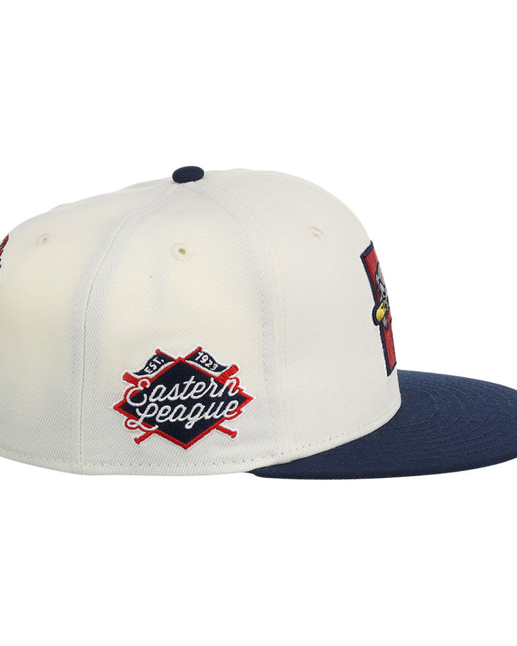 The Ebbets Field Portland Sea Dogs MiLB Snapback Ballcap is a white cap with a navy brim, detailed with a red and navy Eastern League patch featuring crossed bats on the side.