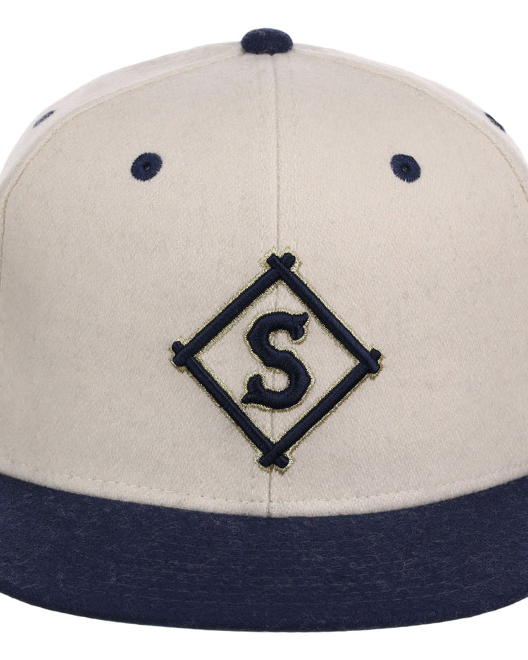 The Ebbets Field Seattle Steelheads NLB Ballpark Fitted Ballcap features a beige crown with navy blue brim and eyelets, plus a diamond-shaped S emblem embroidered on the front.