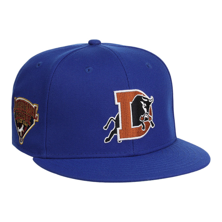 The Ebbets Field Durham Bulls MiLB Snapback Ballcap is a royal blue hat with an orange “D,” black bull logo on the front, and a commemorative patch on the left side.