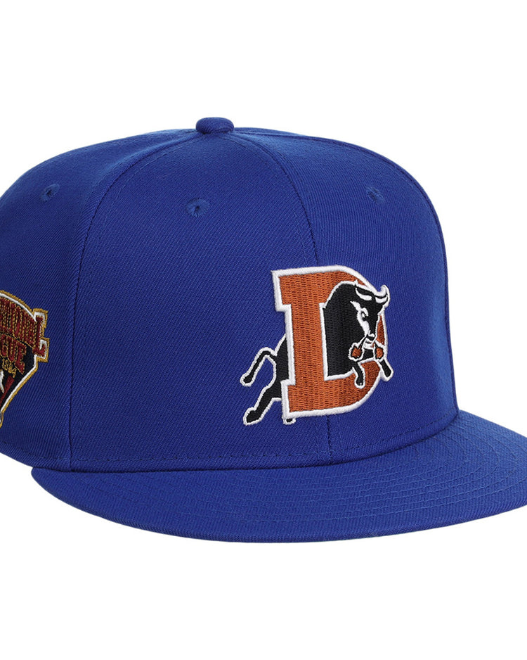 The Ebbets Field Durham Bulls MiLB Snapback Ballcap is a royal blue hat with an orange “D,” black bull logo on the front, and a commemorative patch on the left side.
