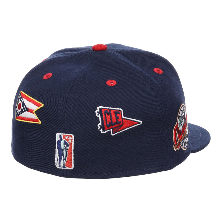 The Ebbets Field Cleveland Buckeyes NLB Varsity Fitted Ballcap is a navy blue cap featuring embroidered patches of the Ohio flag, a red CLE pennant, a baseball player silhouette, and a team logo.