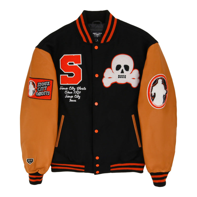 The Ebbets Field Sioux City Ghosts NLB Dna Varsity Jacket is black with orange sleeves and trim, adorned with a red S patch, white skull and crossbones, 