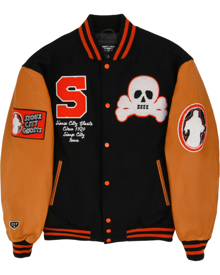 The Ebbets Field Sioux City Ghosts NLB Dna Varsity Jacket is black with orange sleeves and trim, adorned with a red S patch, white skull and crossbones, 