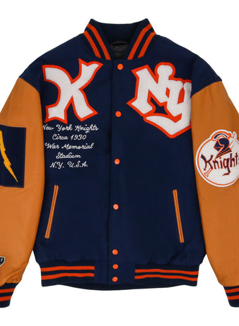 The Ebbets Field New York Knights Dna Varsity Jacket features navy blue and orange colors, NY and Knights patches, a lightning bolt patch on one sleeve, orange-trimmed collar, cuffs and hem, plus embroidered chest text referencing the New York Knights.