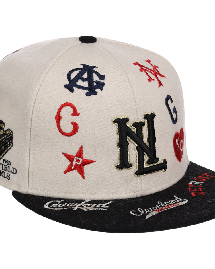 The Ebbets Field Negro League Baseball NLB Ballpark Fitted Ballcap is a white and black cap featuring colorful embroidered Negro League team logos, initials, and symbols on the front, top, and brim.