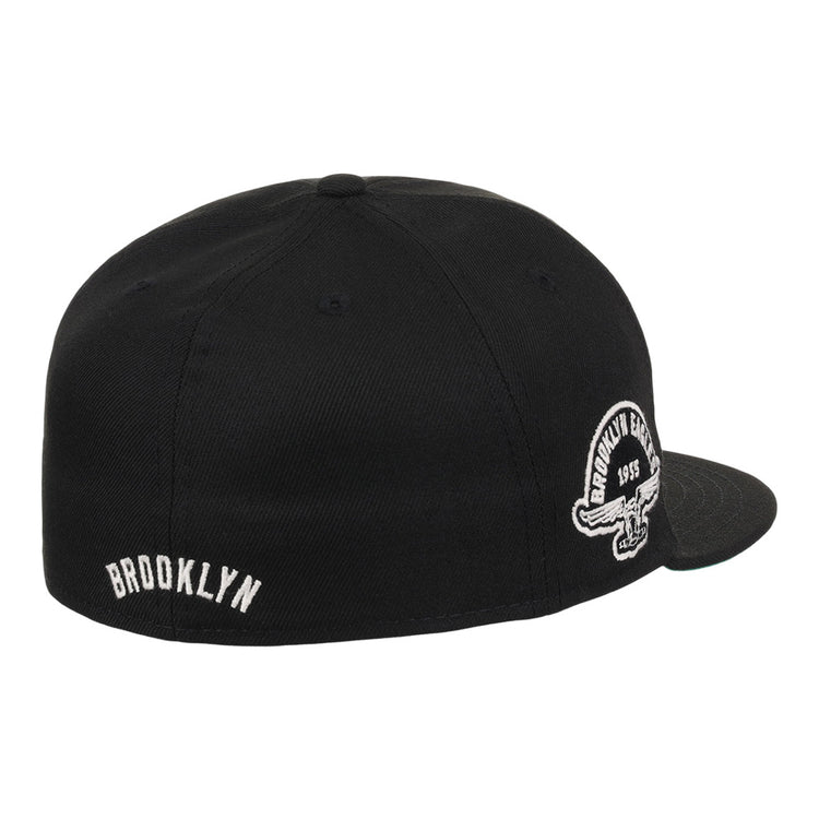 The Ebbets Field Brooklyn Eagles NLB Fitted Ballcap is a black, flat-brim cap featuring BROOKLYN embroidered in white on the back and a circular Brooklyn Eagles logo on the side panel above the ear.