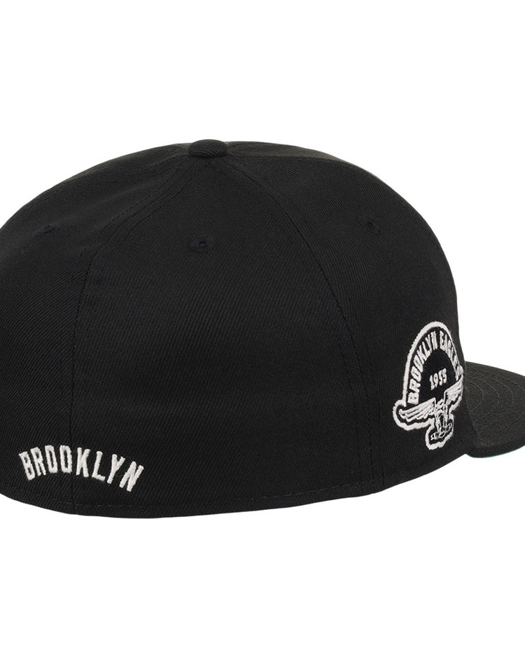 The Ebbets Field Brooklyn Eagles NLB Fitted Ballcap is a black, flat-brim cap featuring BROOKLYN embroidered in white on the back and a circular Brooklyn Eagles logo on the side panel above the ear.