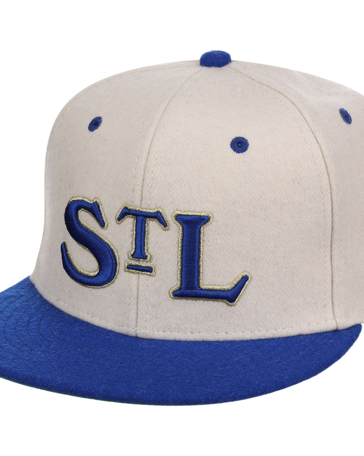 The Ebbets Field St. Louis Stars NLB Ballpark Fitted Ballcap features a beige crown, blue brim and button, and large blue “STL” letters with gold outlines embroidered on the front.