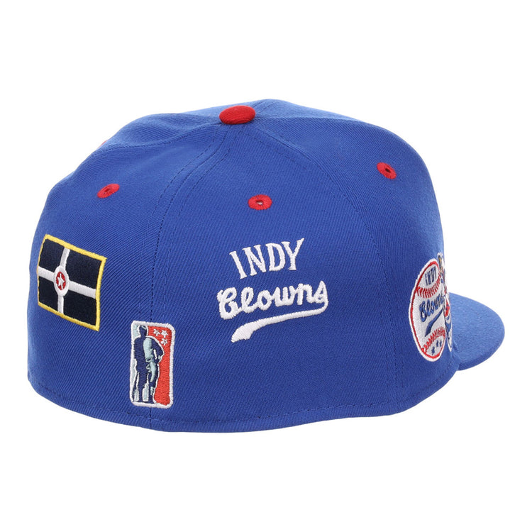 The Ebbets Field Indianapolis Clowns NLB Varsity Fitted Ballcap is a blue cap with red button and stitching accents, plus embroidered patches featuring INDY Clowns, a flag, player silhouette, and “Clowns” round patch.
