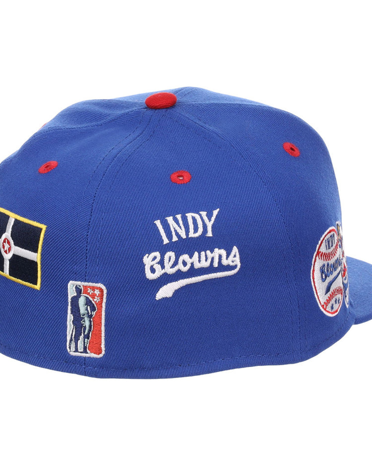 The Ebbets Field Indianapolis Clowns NLB Varsity Fitted Ballcap is a blue cap with red button and stitching accents, plus embroidered patches featuring INDY Clowns, a flag, player silhouette, and “Clowns” round patch.