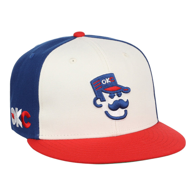 The Ebbets Field Oklahoma City 89Ers MiLB Snapback Ballcap features a white front, blue back, red brim, and a cartoon face with a blue cap embroidered with 