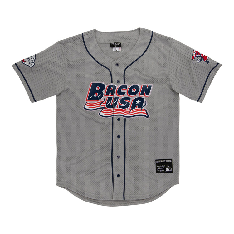The Lehigh Valley Ironpigs MiLB Button Down Jersey by Ebbets Field is a gray baseball jersey with navy trim, “Bacon USA” in red, white, and blue on the front, plus cartoon bacon designs on the left sleeve and right shoulder.