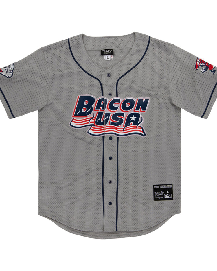 The Lehigh Valley Ironpigs MiLB Button Down Jersey by Ebbets Field is a gray baseball jersey with navy trim, “Bacon USA” in red, white, and blue on the front, plus cartoon bacon designs on the left sleeve and right shoulder.