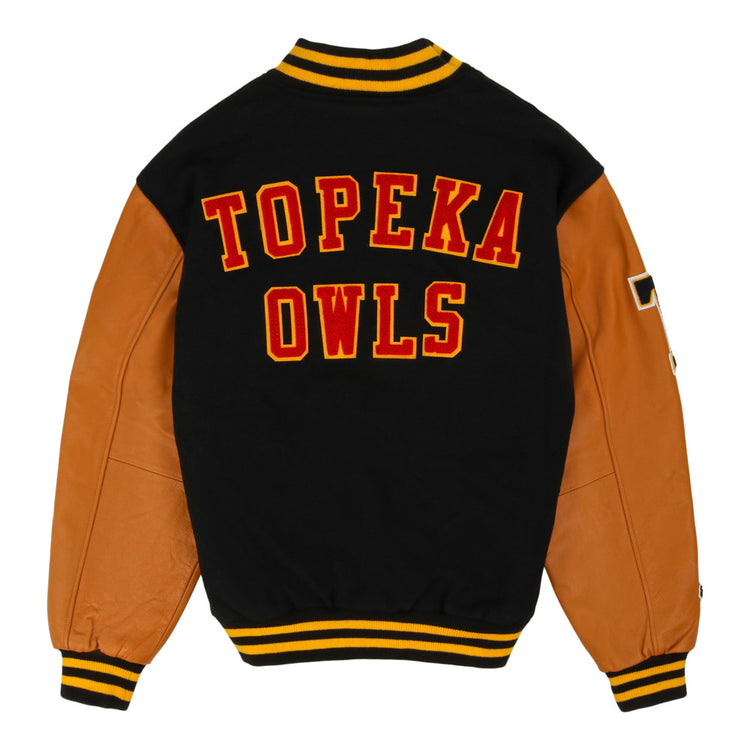 The Ebbets Field Topeka Owls MiLB Dna Varsity Jacket features a black wool body, tan leather sleeves, yellow-black striped trim, and bold red and yellow 