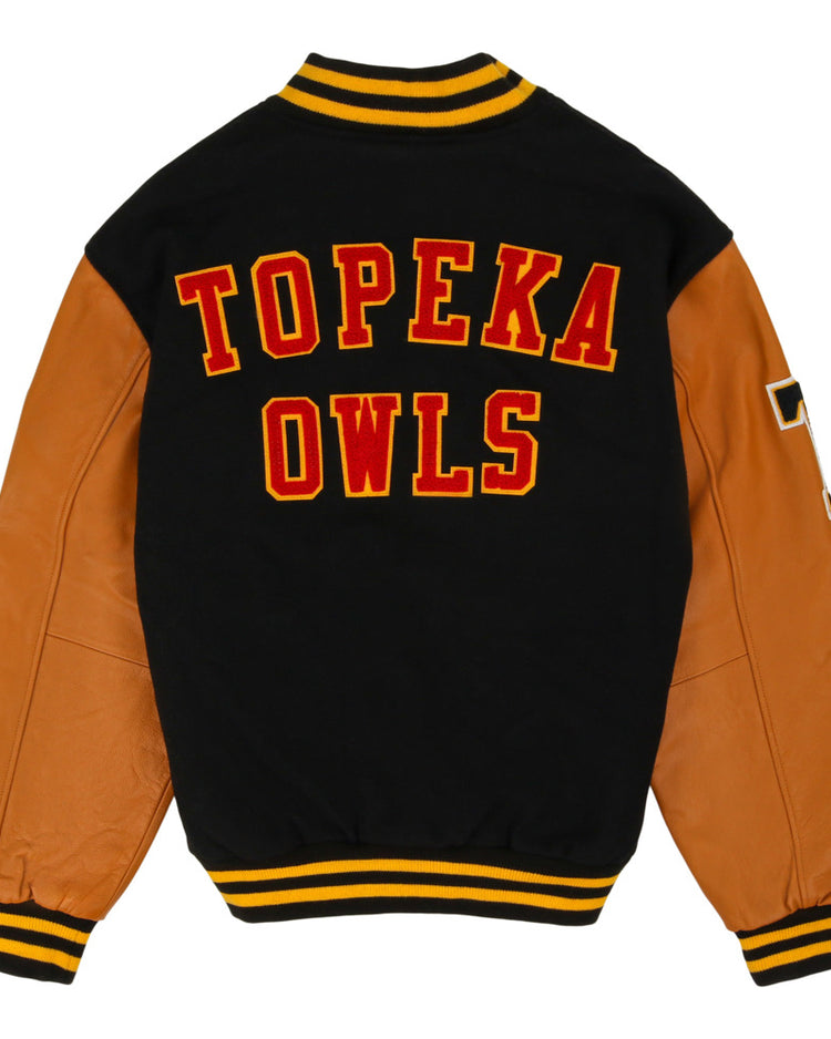 The Ebbets Field Topeka Owls MiLB Dna Varsity Jacket features a black wool body, tan leather sleeves, yellow-black striped trim, and bold red and yellow 
