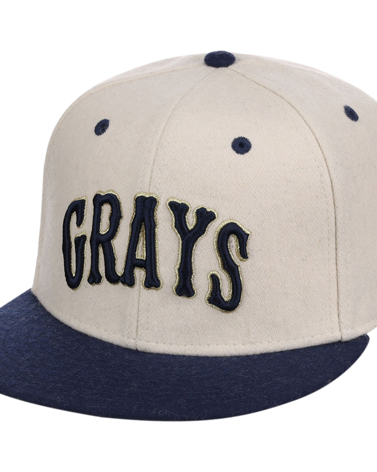 The Ebbets Field Homestead Grays NLB Ballpark Fitted Ballcap features a beige crown, dark blue brim, button, and eyelets, with 