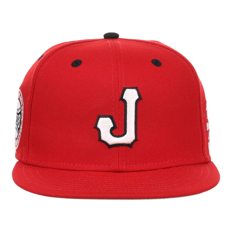 The Ebbets Field Jacksonville Red Caps NLB Varsity Fitted Ballcap is red with a white J outlined in black on the front, flat brim, black ventilation holes on top, and side patches.