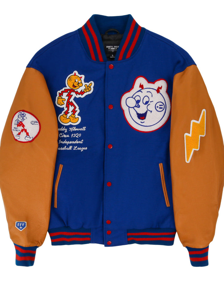 The Ebbets Field Reddy Kilowatt DNA Varsity Jacket is blue and orange, with cartoon baseball patches, smiling baseball faces, a lightning bolt, and an “Officially Licensed Cooperstown Baseball League” patch.