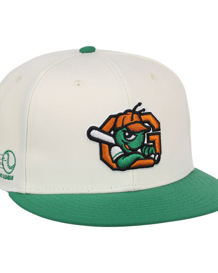 The Ebbets Field Greensboro Grasshoppers MiLB Snapback Ballcap is a white cap with a green brim and button, featuring an embroidered cartoon insect with a bat on the front and green Minor League branding on the side.