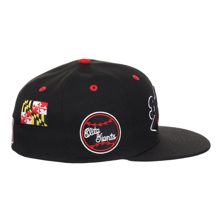 The Ebbets Field Baltimore Elite Giants NLB Varsity Fitted Ballcap is a black cap with red accents, red and white embroidered Elite Giants logo, Maryland state flag on the side, and embroidered patches. Shown in a side view.