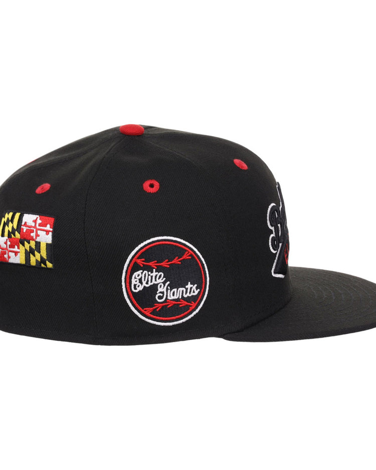 The Ebbets Field Baltimore Elite Giants NLB Varsity Fitted Ballcap is a black cap with red accents, red and white embroidered Elite Giants logo, Maryland state flag on the side, and embroidered patches. Shown in a side view.