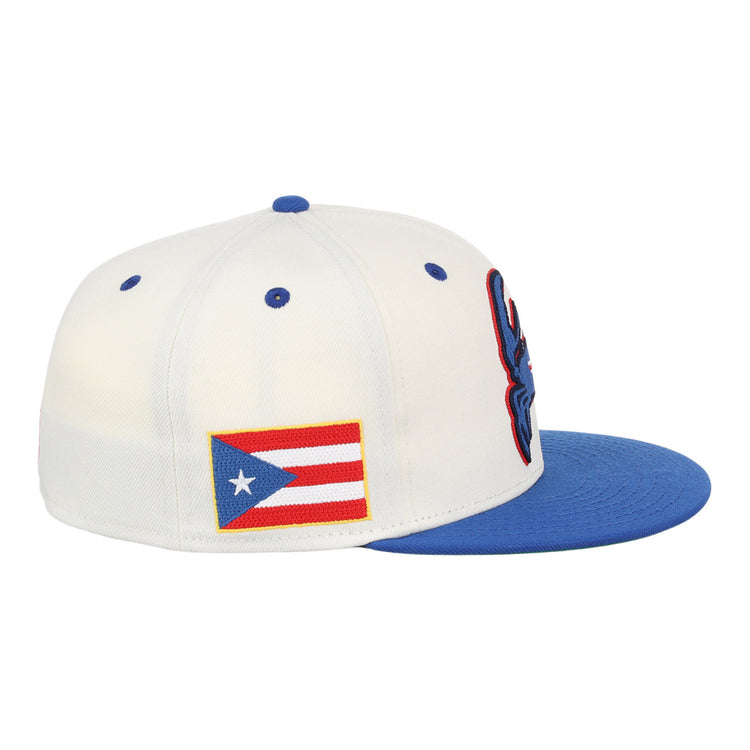 The Ebbets Field Santurce Cangrejeros Chainstitch Fitted Ballcap is a white hat with a blue brim, blue embroidered front details, and a Puerto Rican flag patch on the side.