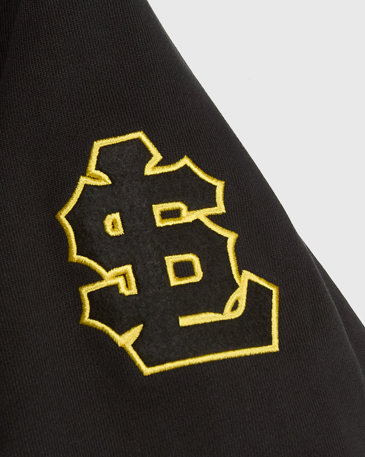 Close-up of a black cotton Salt Lake Bees Heavyweight Cotton Terry Pullover Hoodie sleeve featuring an embroidered yellow and black logo of the letters SL intertwined.