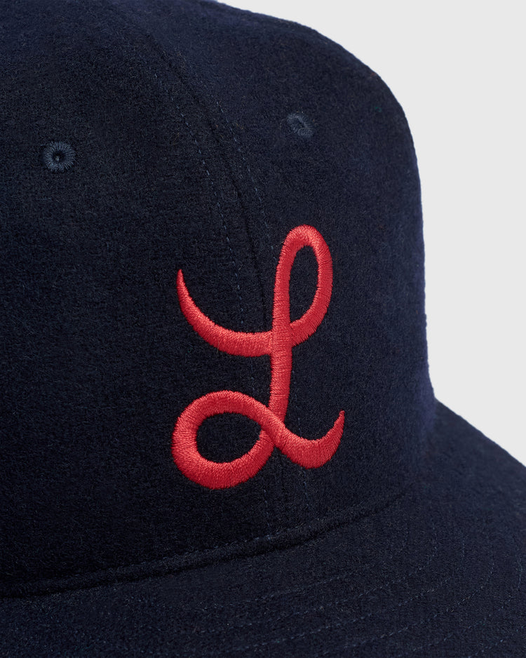 Close-up of a navy wool Mystery Caps of Mexico – La Junta de Nuevo Laredo 1940 Wool Ballcap by Ebbets Field, featuring an embroidered red cursive L on the front crown.