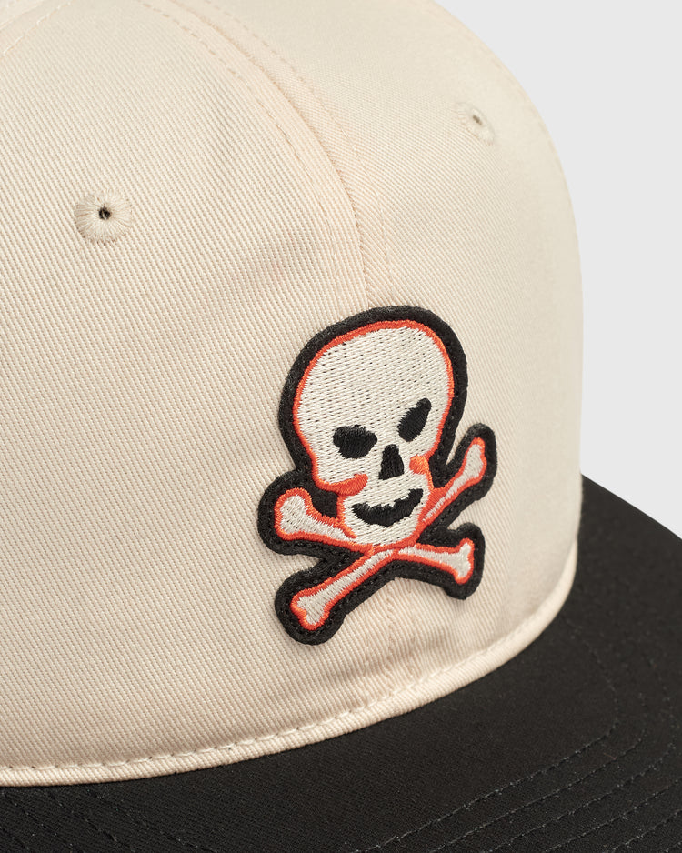 Sioux City Ghosts Cotton Twill Ballcap in off-white with a black brim and an embroidered skull and crossbones patch in white, orange, and black.