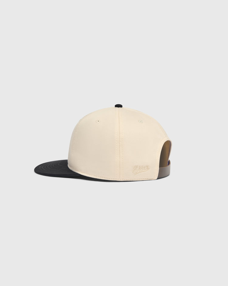 Side view of an Ebbets Field Sioux City Ghosts Cotton Twill Ballcap featuring a cream-colored crown, a black brim, and a small black button on top.